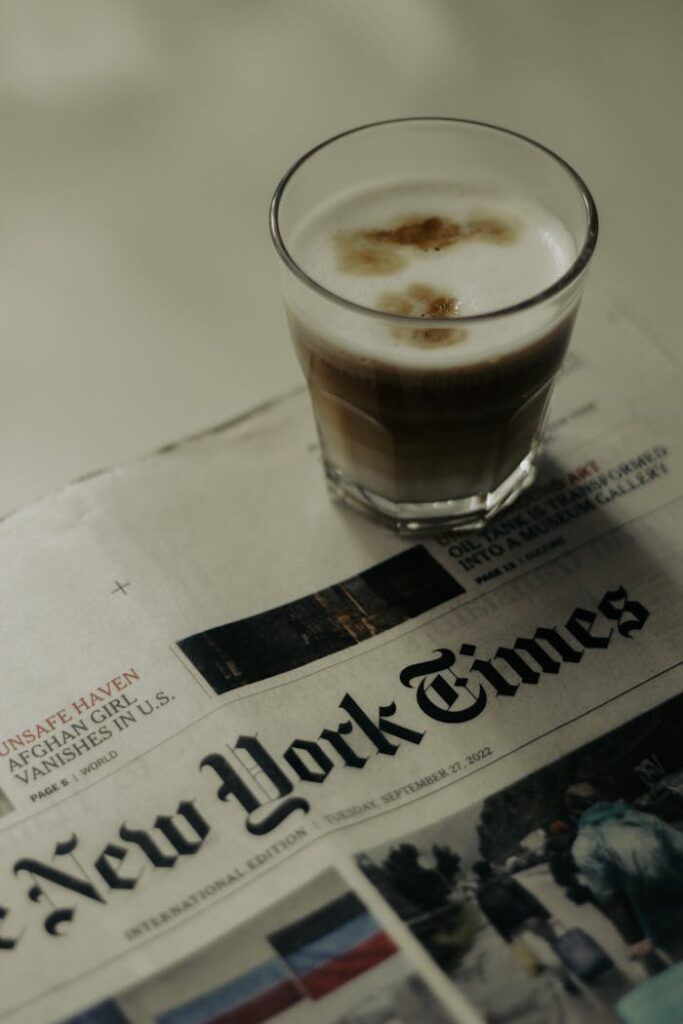 A latte sits on a table beside a New York Times newspaper, creating a tranquil morning atmosphere.