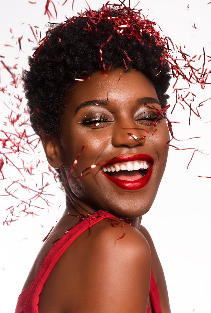 Radiant woman smiling amidst red confetti celebrating New Year's cheer.